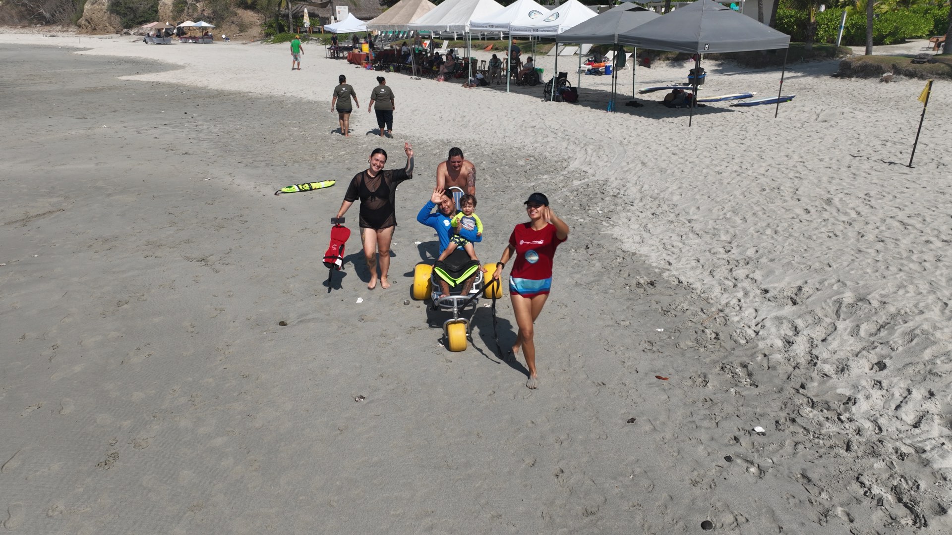 Familia y voluntarias de la fundación acompañando a un niño en silla anfibia en la playa